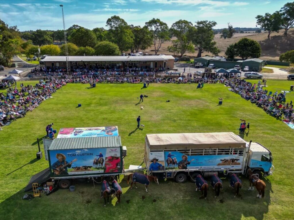 An aerial view of the Tom Curtain show in Mt Pleasant with the audience seated around a large square of grass and Tom's animal trailer in the front.
