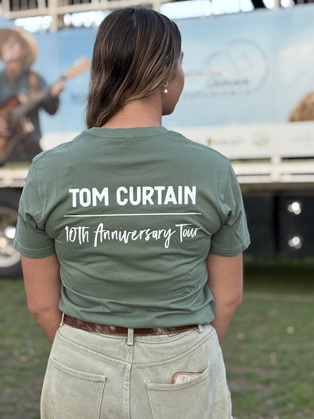 HeresToYouTeeAdult-back Tom Curtain crew member Hannah showcasing the back of the Here's To You Anniversary T-shirt