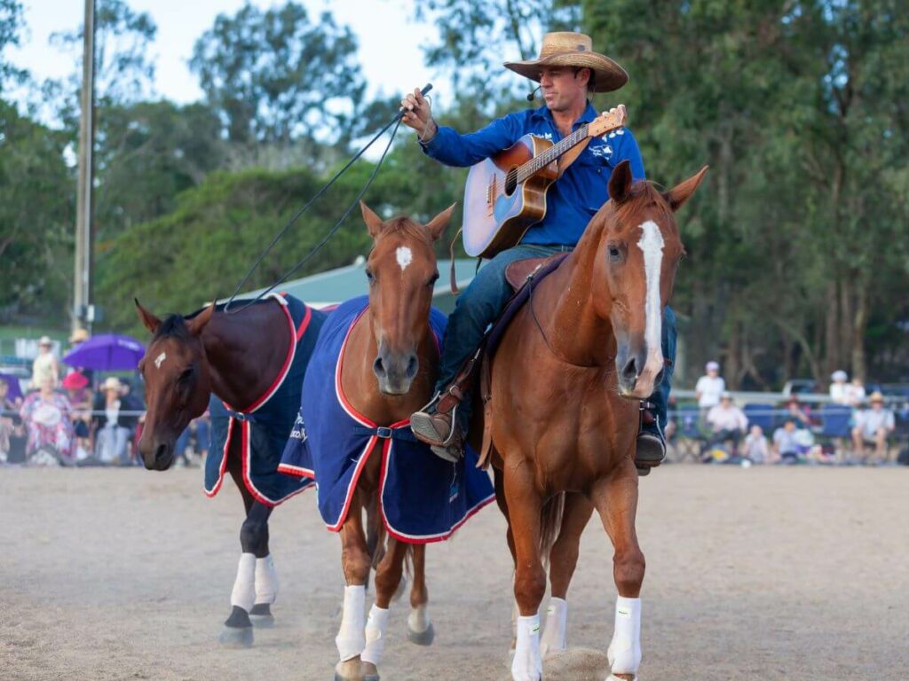 Tom Curtain with his guitar on a horse leading other horses